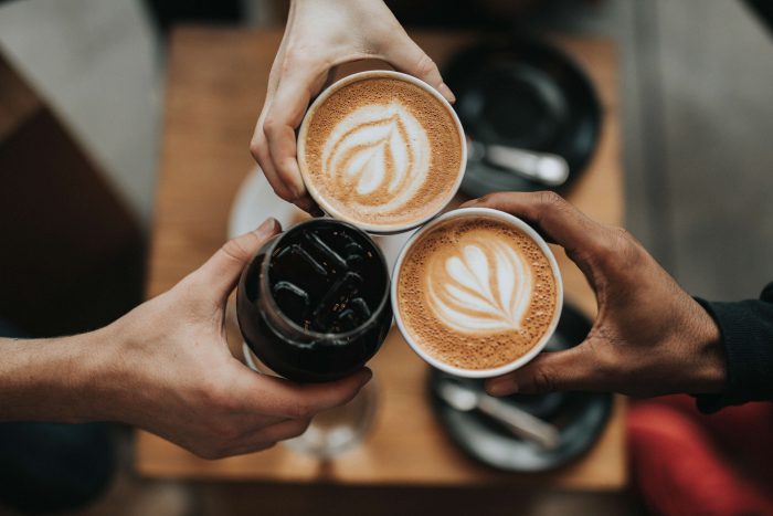 A photo of three people holding a different coffee drinks. The photo is taken from above