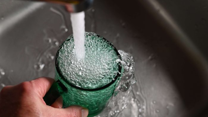 A photograph of a fast stream of clean water flowing from a kitchen tap into an overfilled green glass