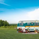 An image of a cute white, green, and yellow caravan parked in a field.