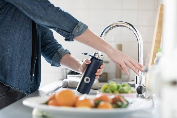 An image of a man standing at a kitchen bench filling up a water bottle from a tap