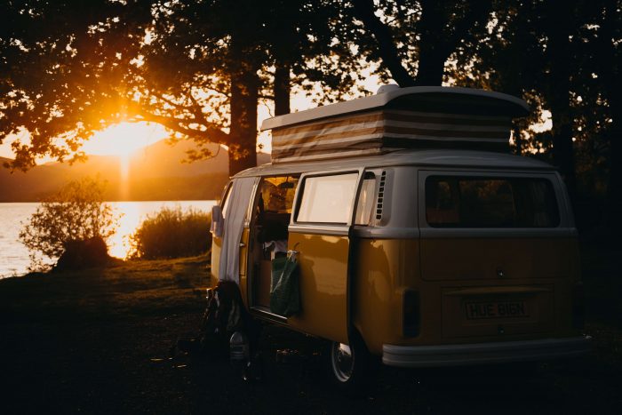An image showing a yellow and white combi van parked in front of a lake at sunset