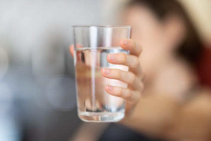 An image of a glass of water which has been filtered by carbon. 
 The glass is being held out by a person